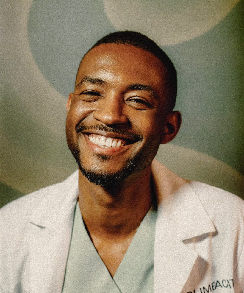 Portrait of a smiling physician in a white coat over scrubs.